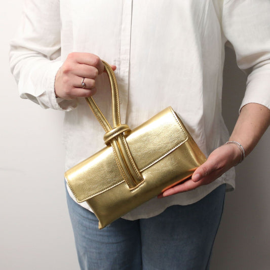 Person holding a gold handbag against a plain background