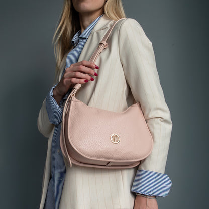 Soft pink pebbled leather Hoblò hobo bag with a gold logo carried over the shoulder by a model in a cream pinstripe blazer