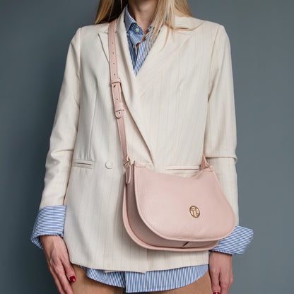 Blush pink Hoblò soft leather hobo bag with an adjustable strap worn crossbody against a cream blazer and blue striped shirt