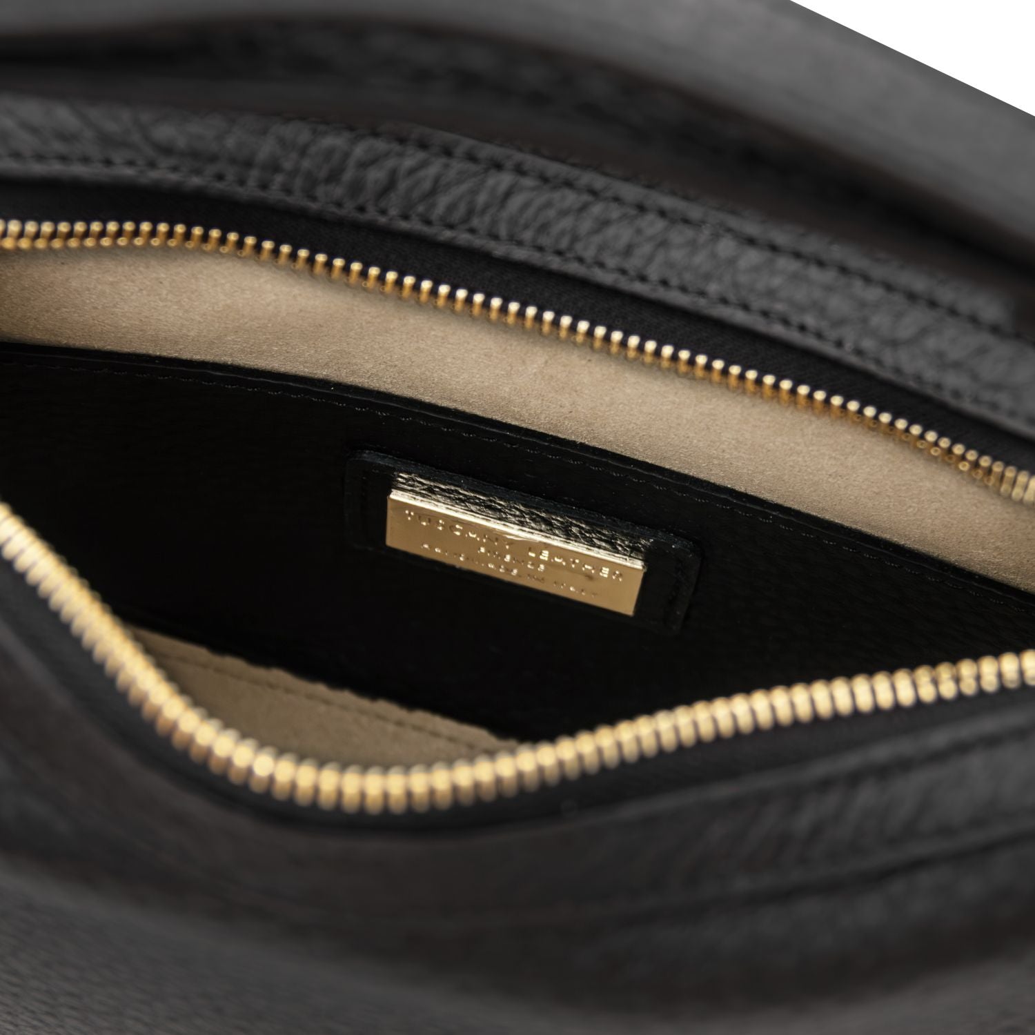Interior close up of the black Hoblò bag showing the gold zipper and a gold logo plaque on the lining