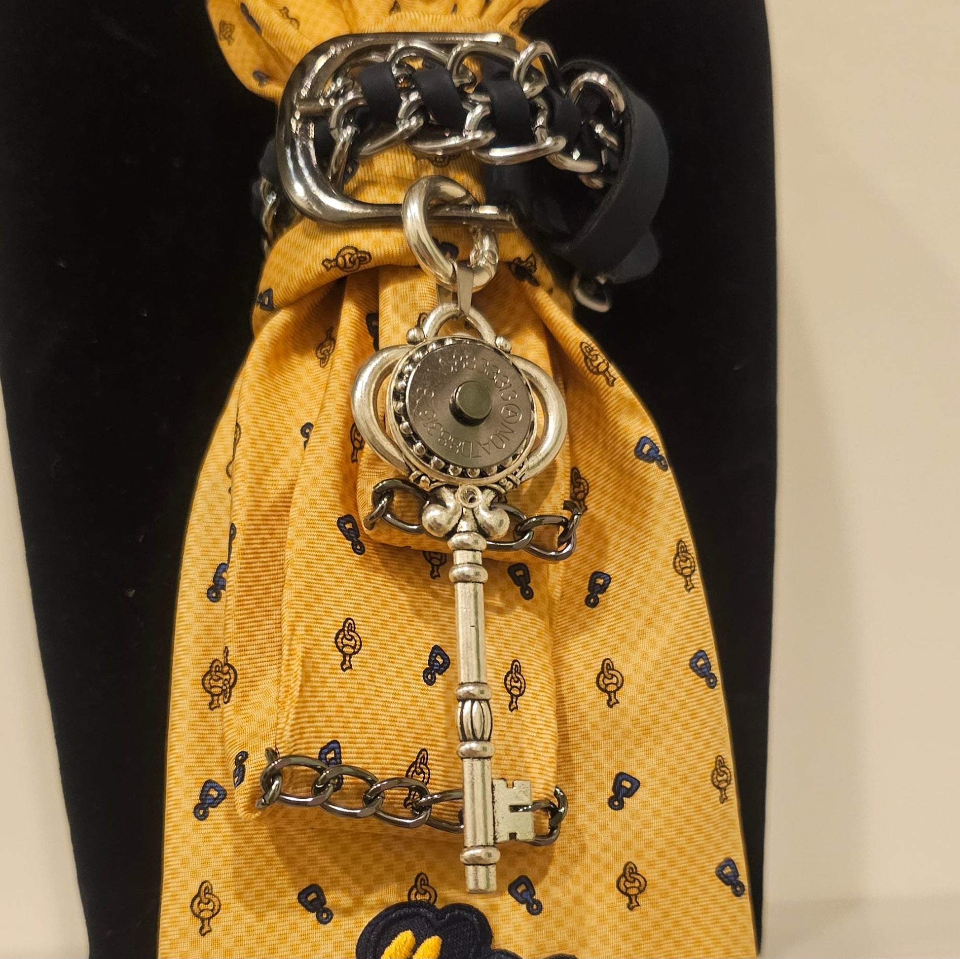 Close-up of yellow tie showing I can and I will patch and a silver key pendant attached to layered chains