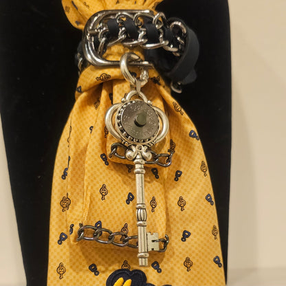Close-up of yellow tie showing I can and I will patch and a silver key pendant attached to layered chains