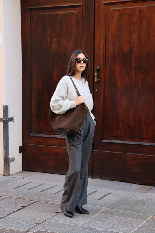 Model wearing sunglasses carries a large brown Elsa suede leather boat tote against a wooden door.