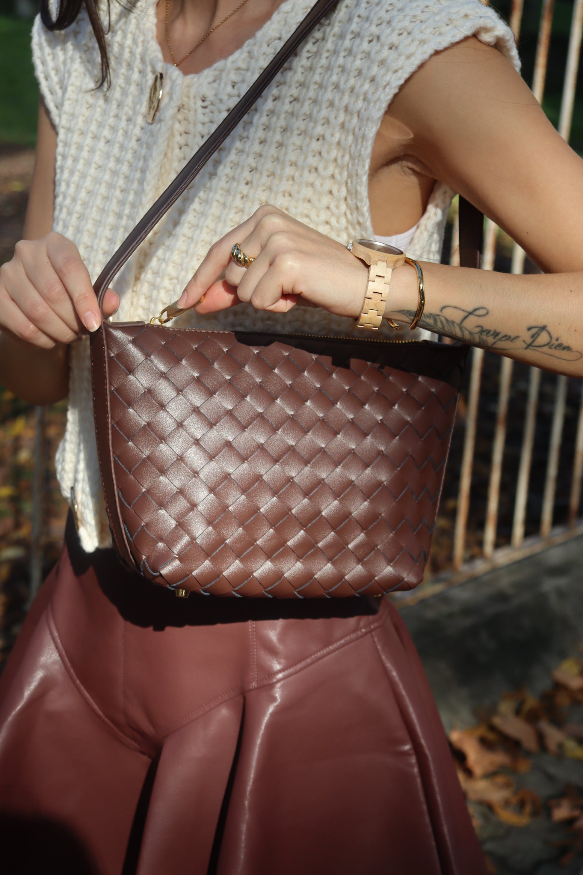 Model carries a brown woven leather boxed pouch bag with a long shoulder strap against a white knit top