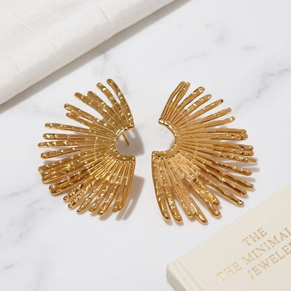 Gold fan-shaped earrings on a white surface with a jewelry box in the background.