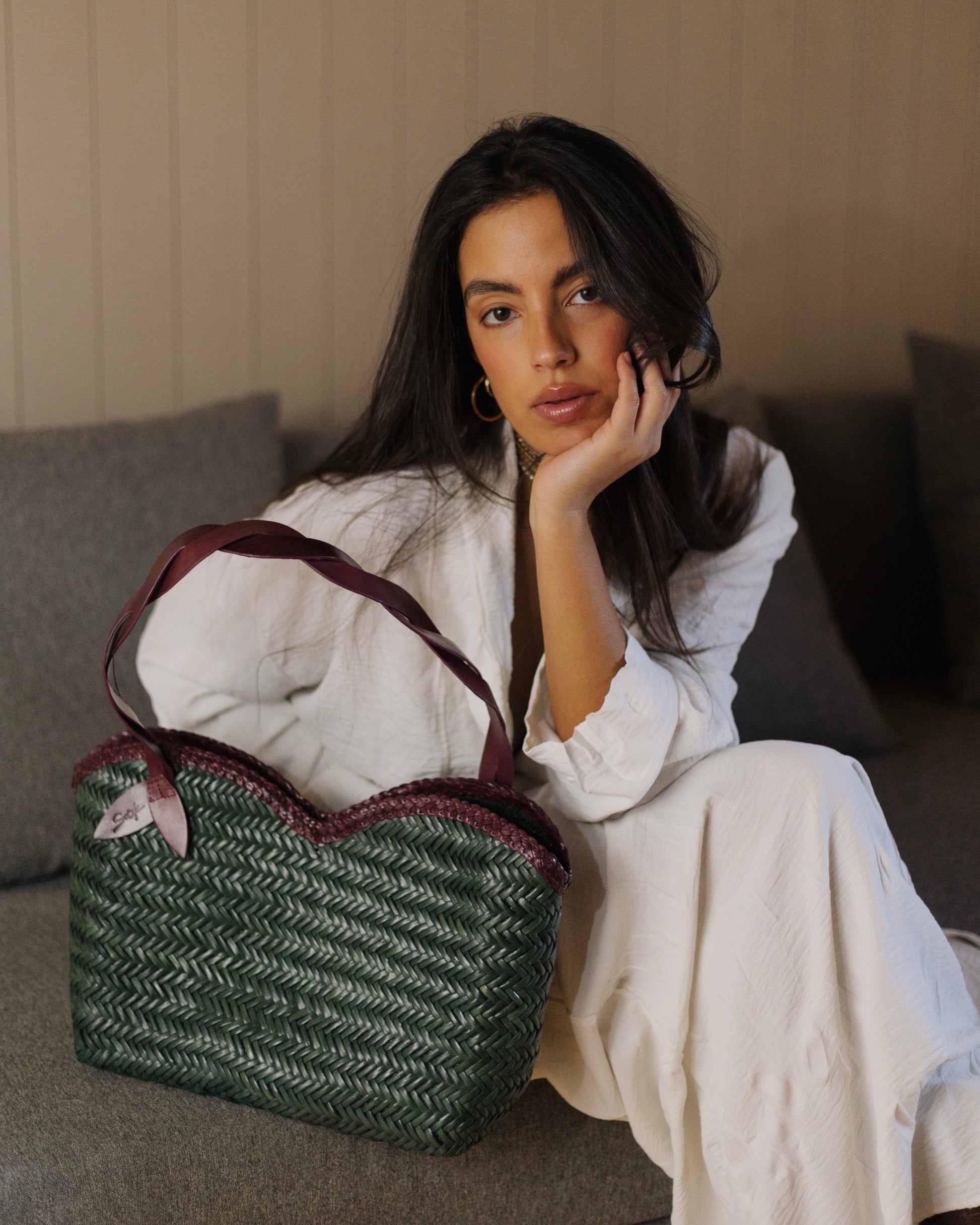 Léafa - Handwoven Leather Shoulder Bag | Burgundy & Green showing a woven green leather body with burgundy leather handles and trim placed on a couch.