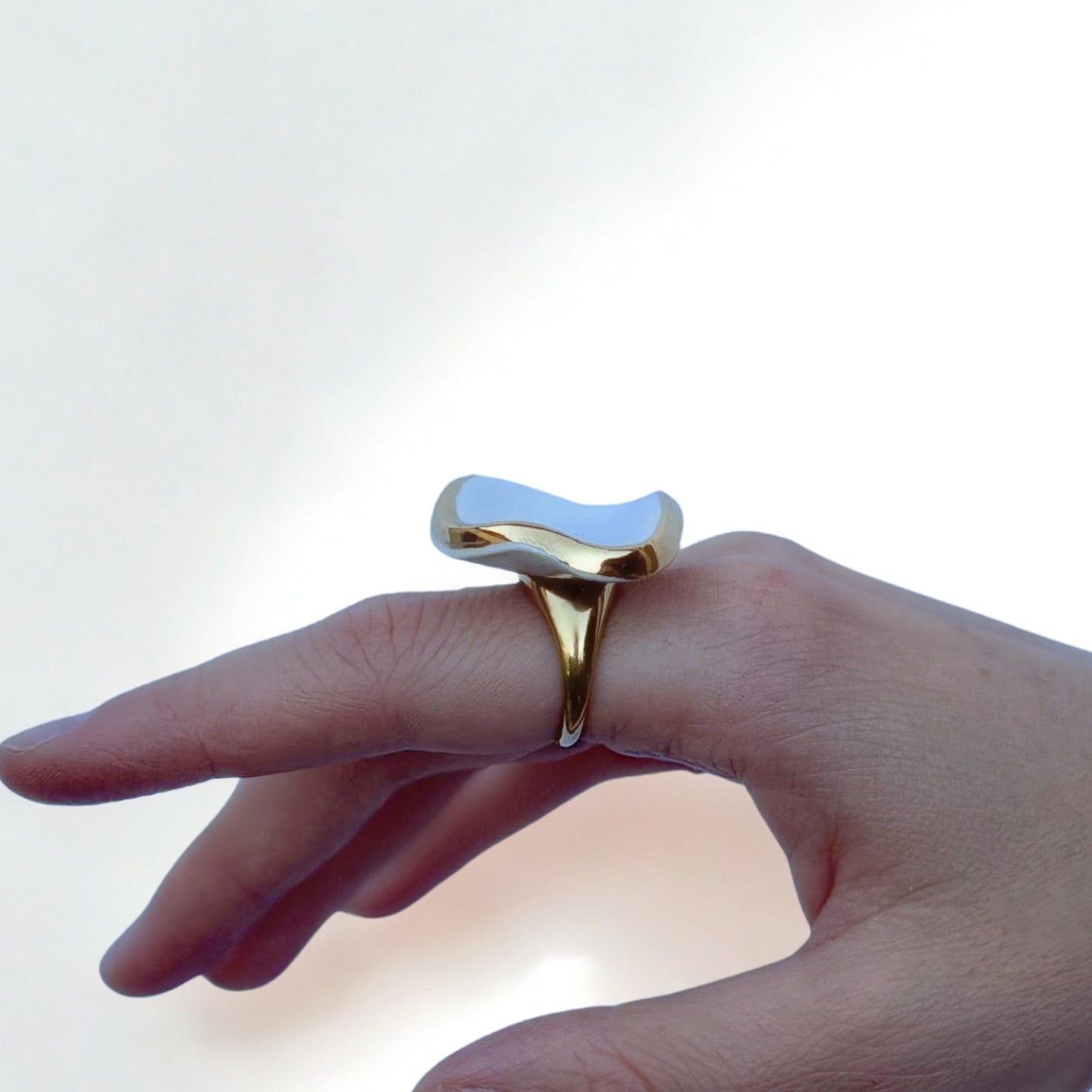 Gold ring with a glossy white irregular ceramic top worn on a finger