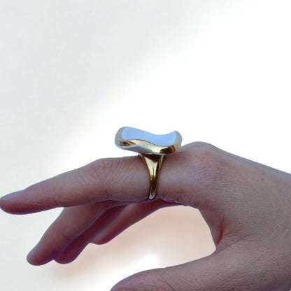Gold ring with a glossy white irregular ceramic top worn on a finger