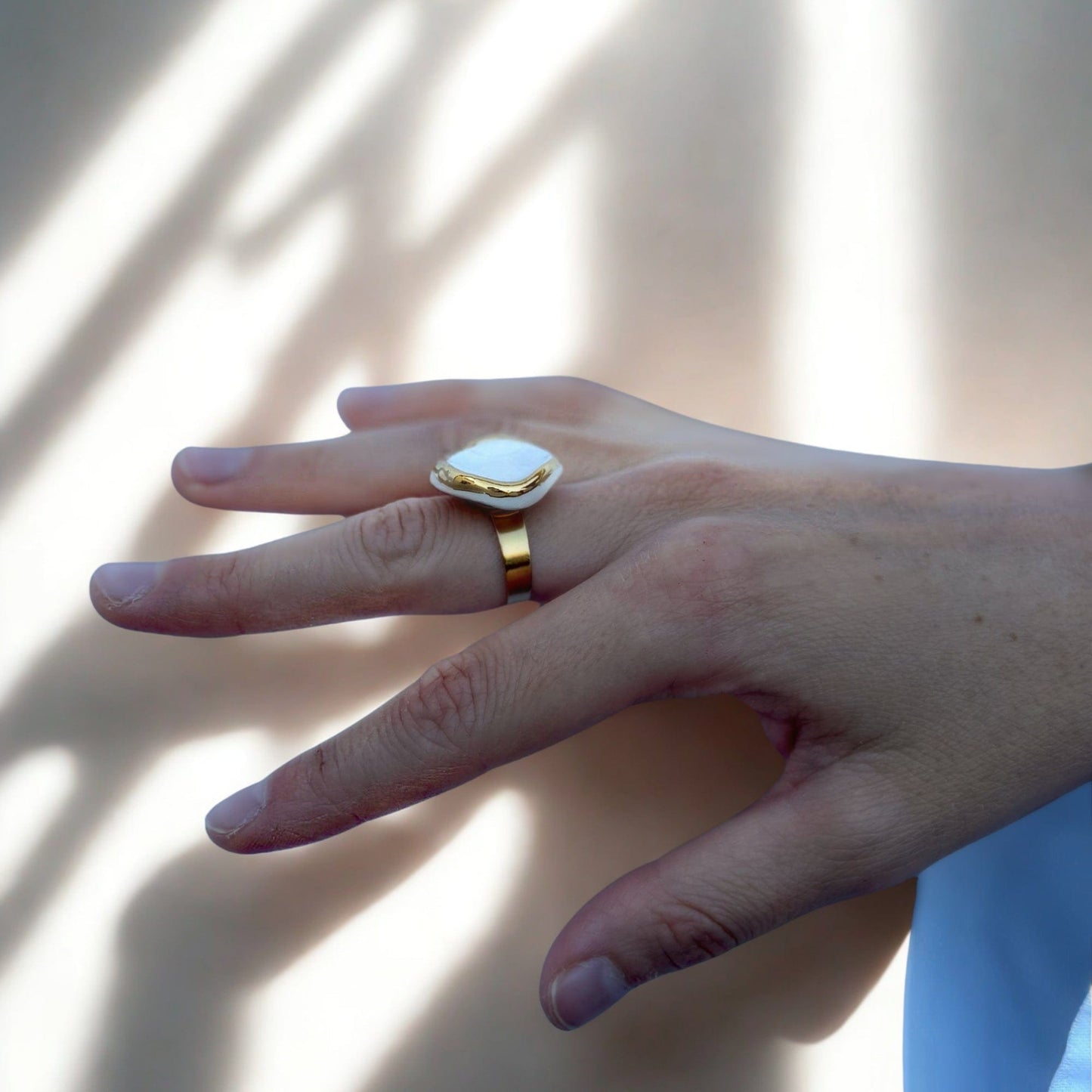 Side view of a gold ring with a white ceramic top on a finger