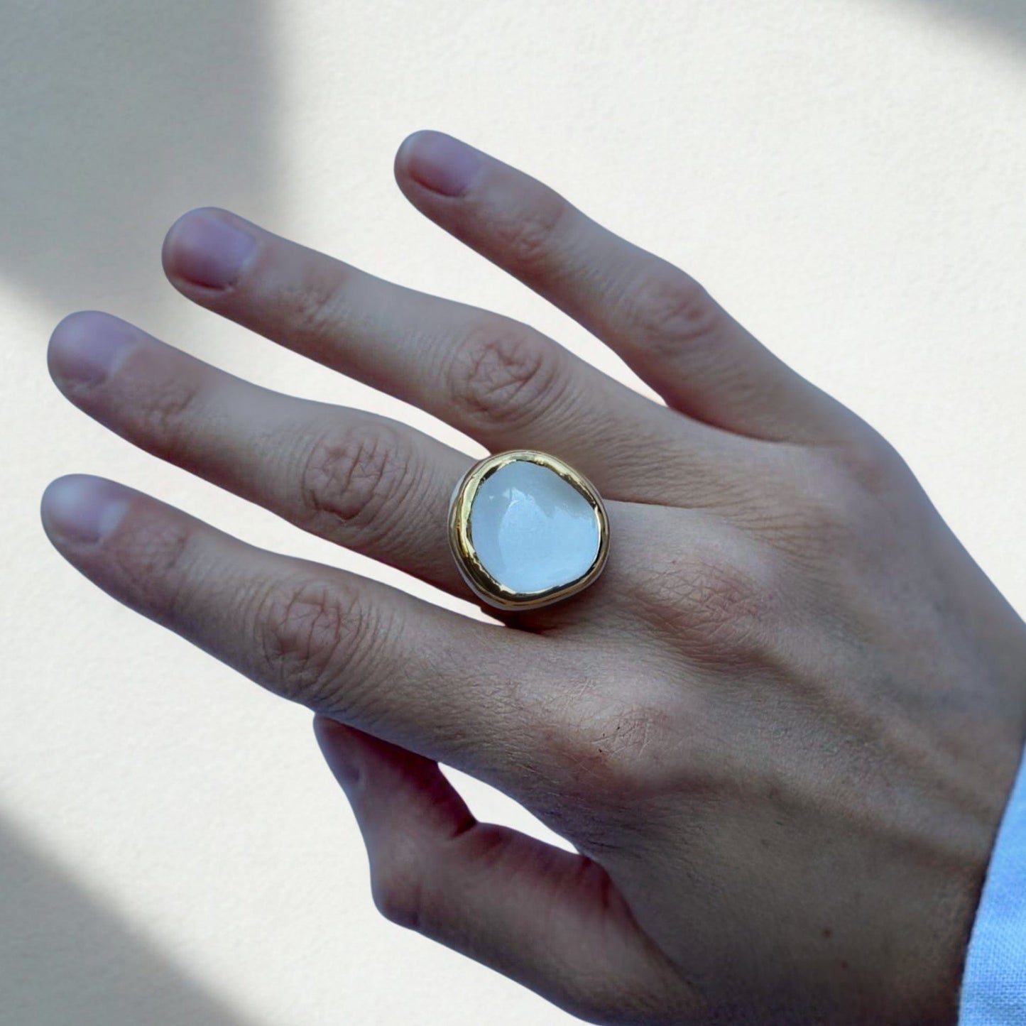 Close-up of a gold band ring featuring a white ceramic top on a finger