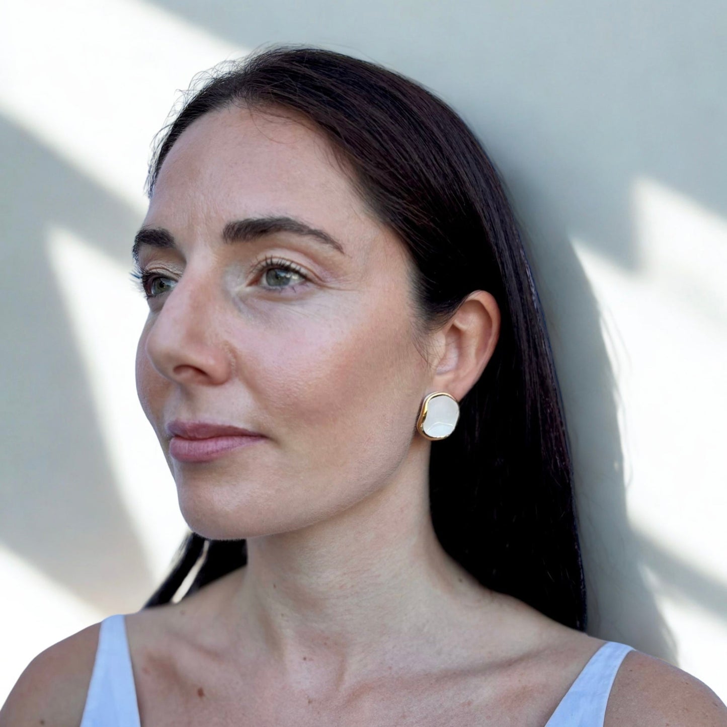 Woman wearing white and gold ceramic earrings with a white top with a neutral background