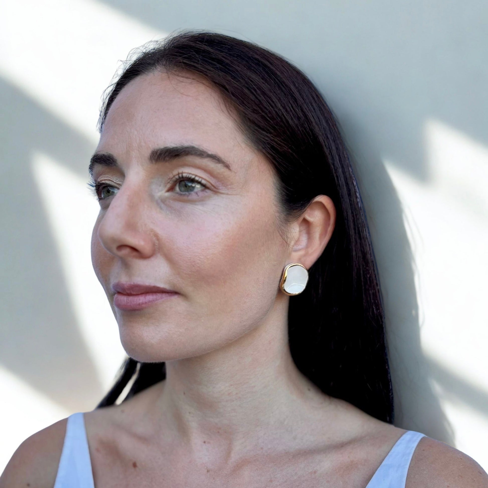 Woman wearing white and gold ceramic earrings with a white top with a neutral background