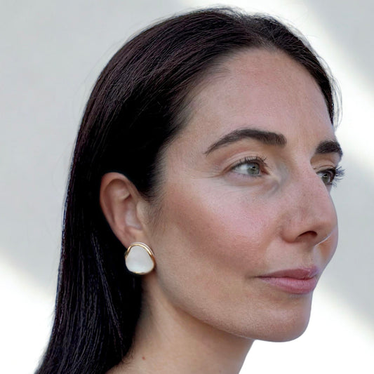 Close up of a woman wearing Leda white ceramic stud earrings with gold luster