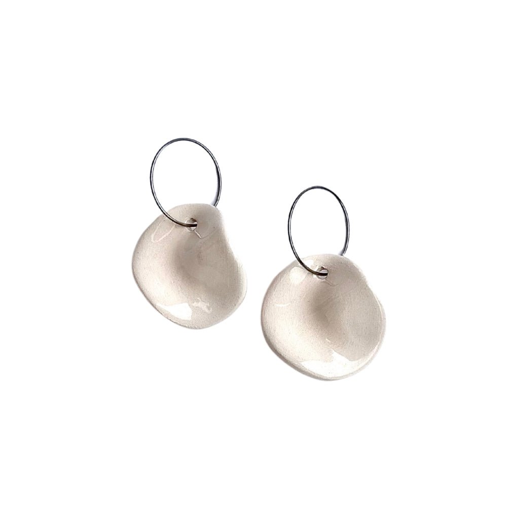 Pair of white ceramic dangle earrings with irregular circular discs on silver hooks against a white background
