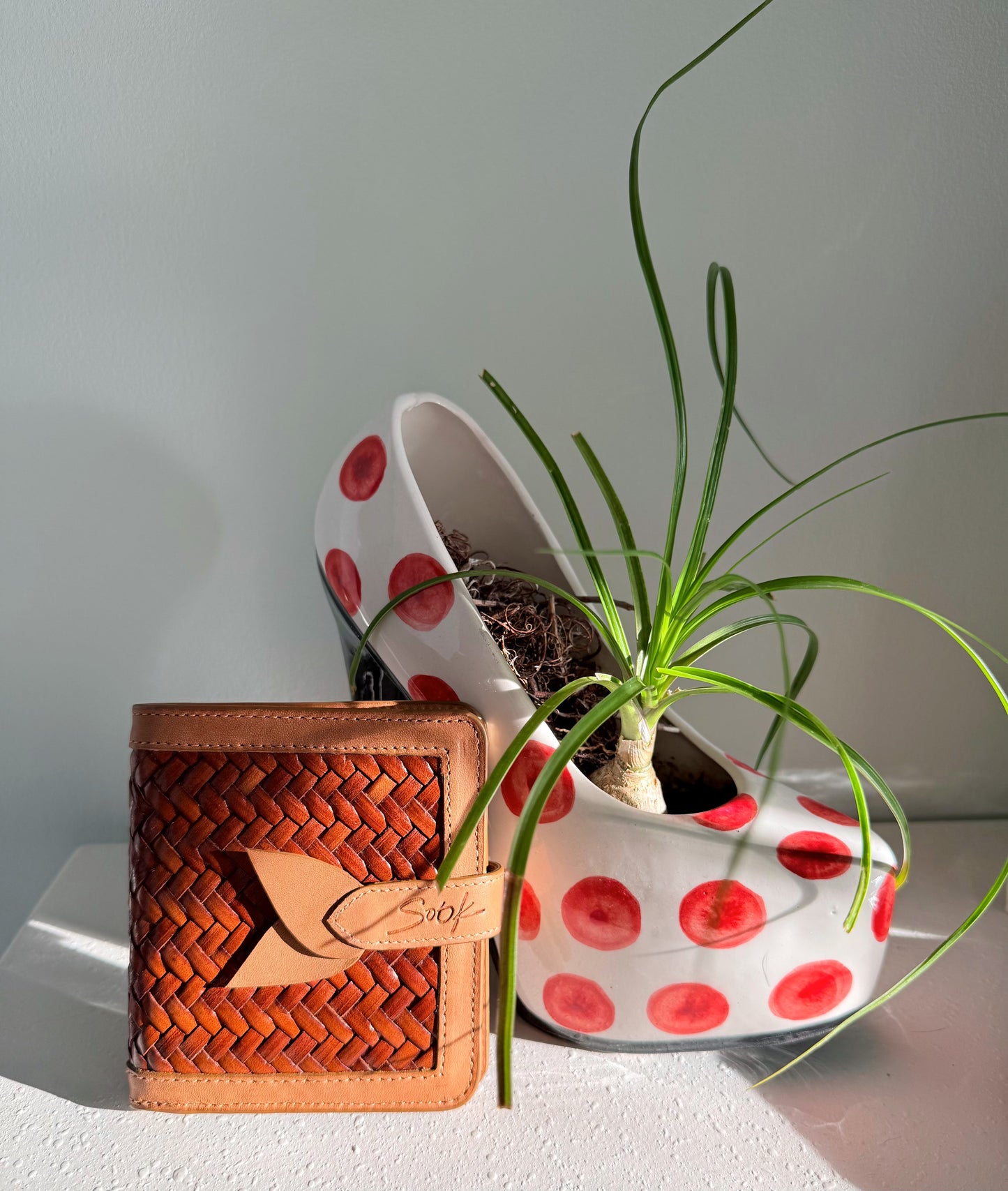 Lumi - Handwoven Leather Wallet | Taupe & Coffee featuring woven leather texture with smooth taupe leather trim beside a white planter with red dots and green plant