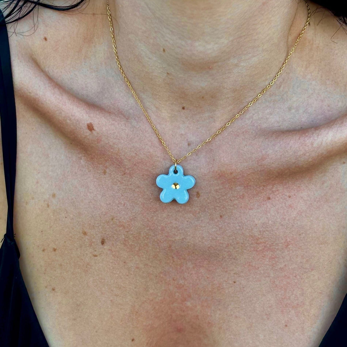 Light blue flower ceramic pendant with a gold center on a gold chain