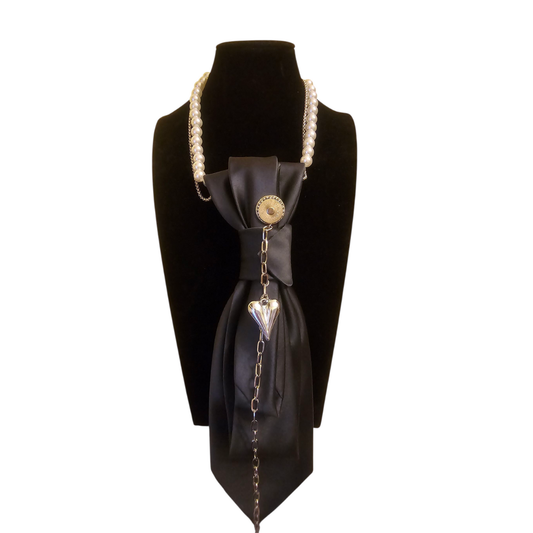 Pearl necklace with a satin black bow centerpiece and a dangling heart pendant on a display bust