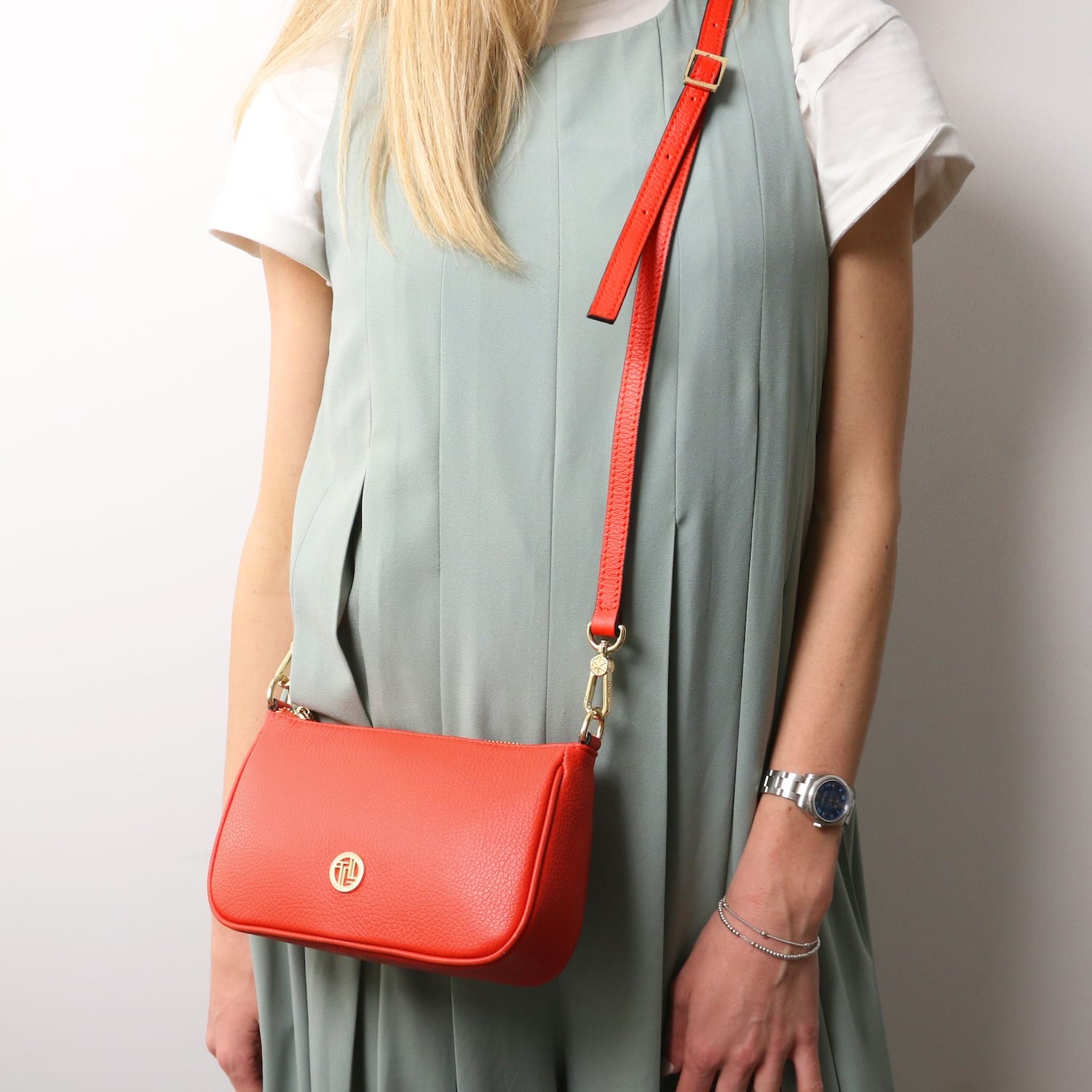 Red leather Parfait clutch with matching red strap worn crossbody by a model in a sage green dress