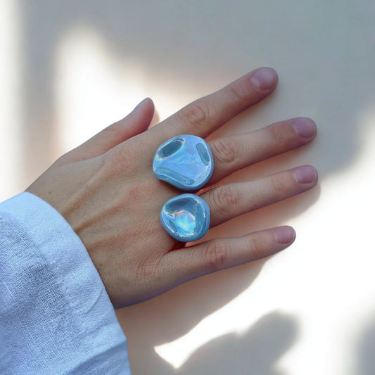 Two light blue pearl ceramic rings worn on a hand against a pale background.