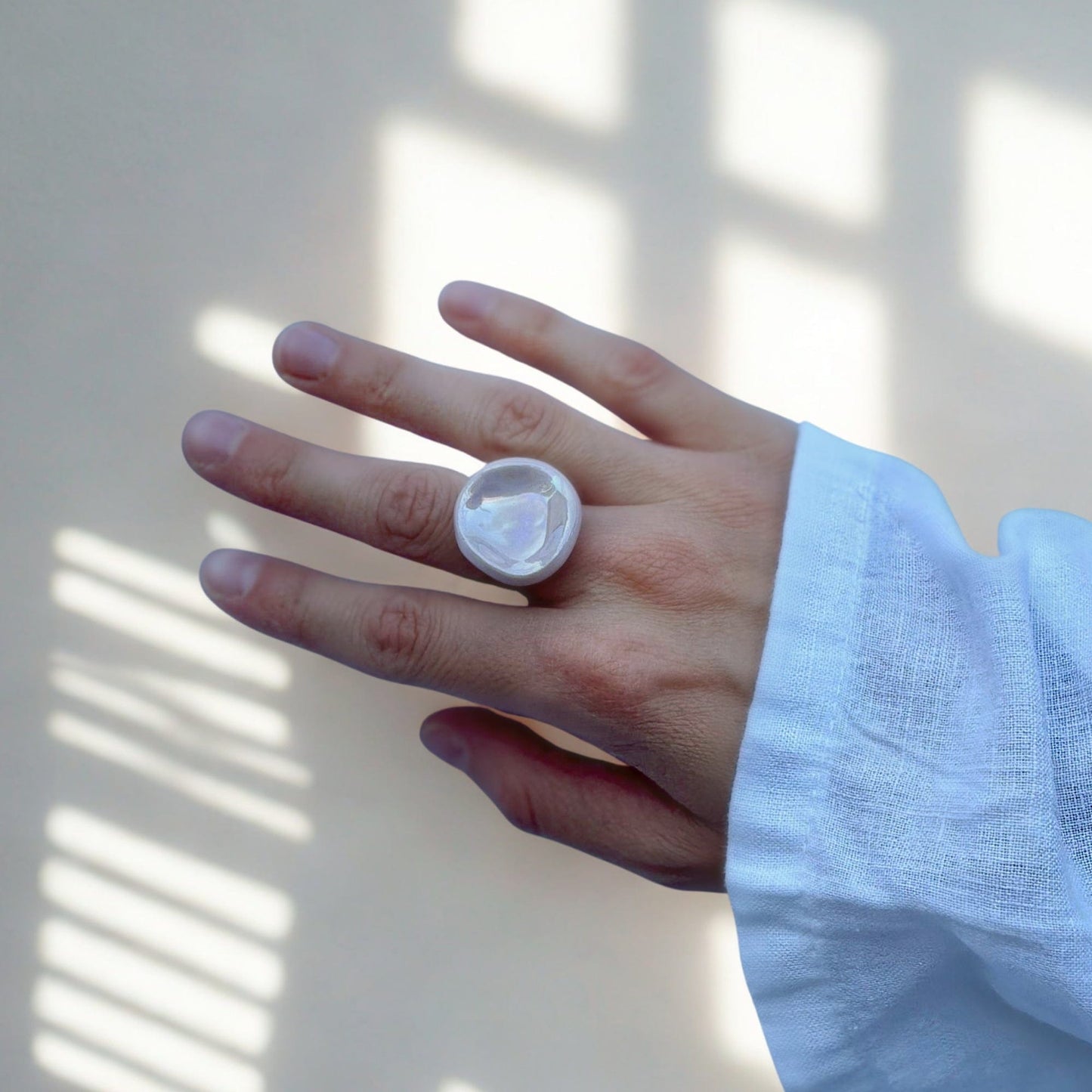 Close up of a hand wearing a round pearl pink ceramic ring from the Perla collection