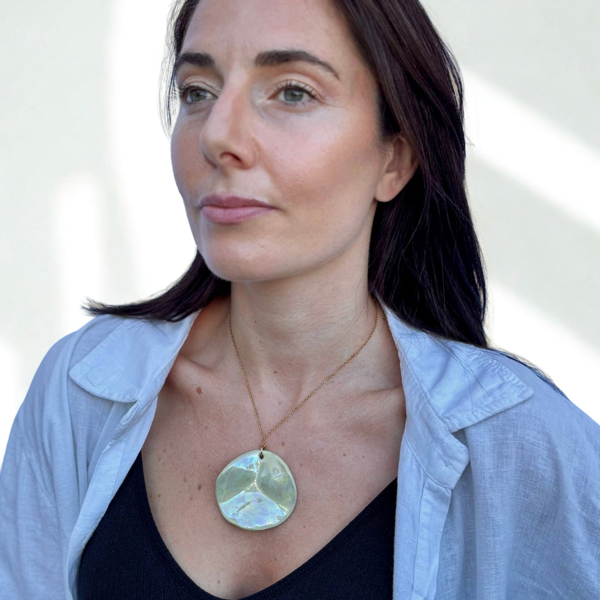 Model wearing a large round sage green ceramic pendant necklace on a delicate gold chain.