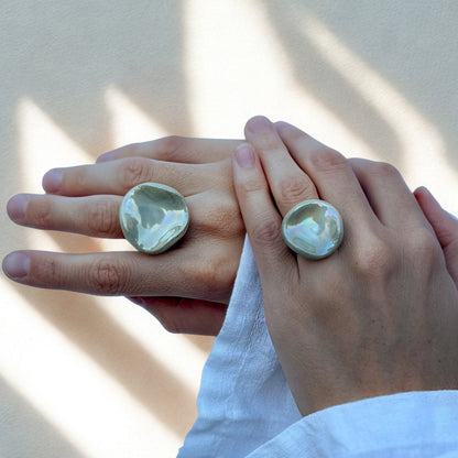 Two hands wearing large sage green pearl ceramic Perla rings on adjacent fingers
