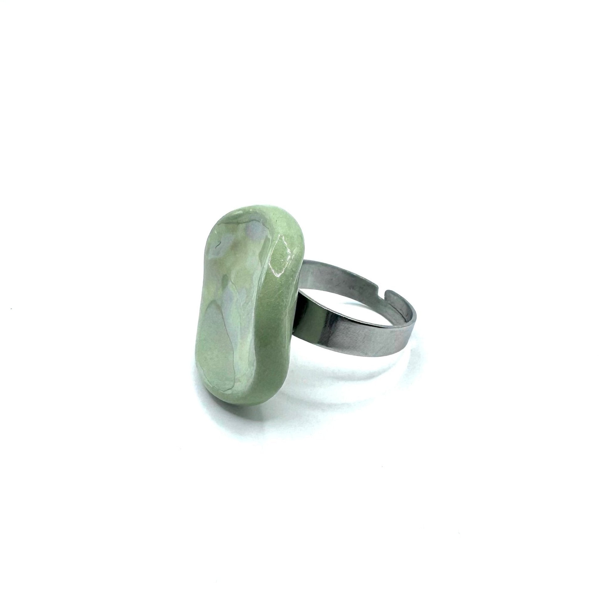Close up of a single sage green pearl ceramic Perla ring on a finger with a metallic band
