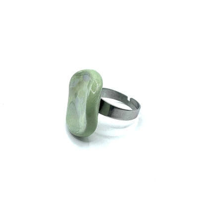 Close up of a single sage green pearl ceramic Perla ring on a finger with a metallic band