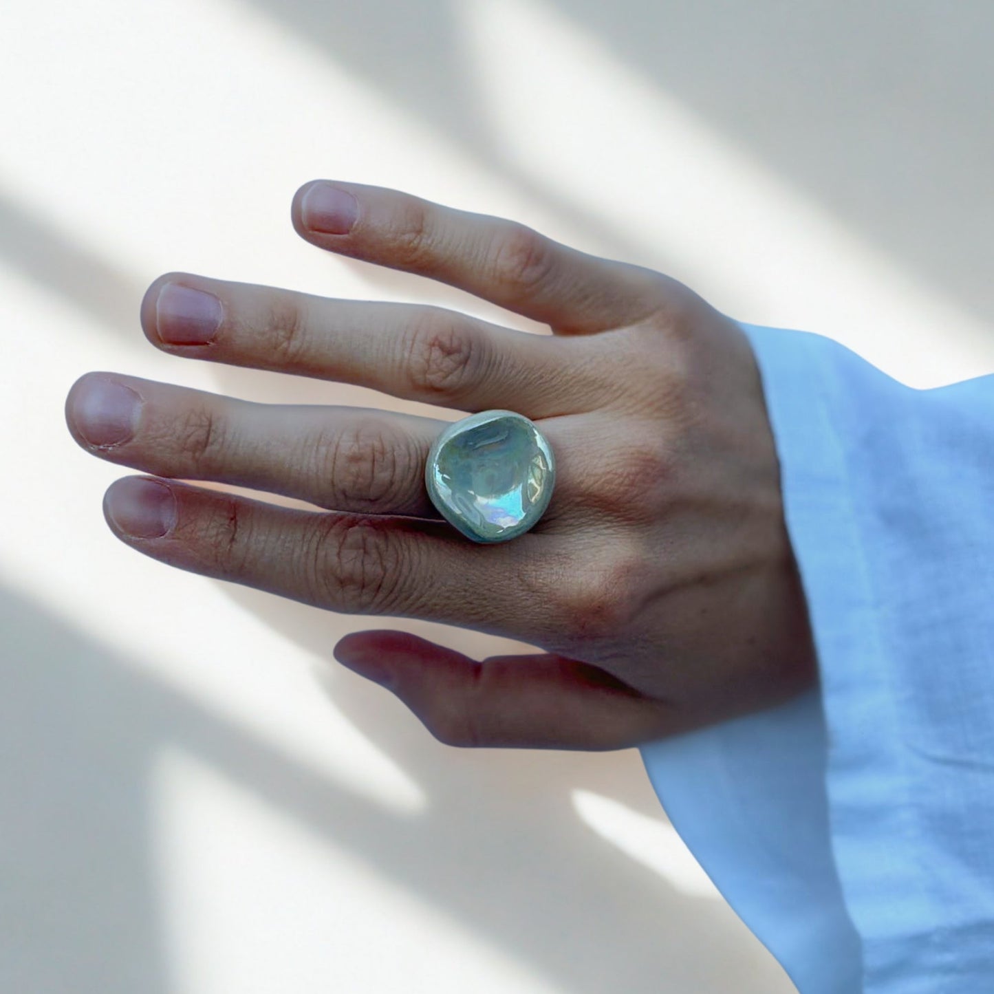 Close up of a sage green pearl ceramic Perla ring on a finger against a light background
