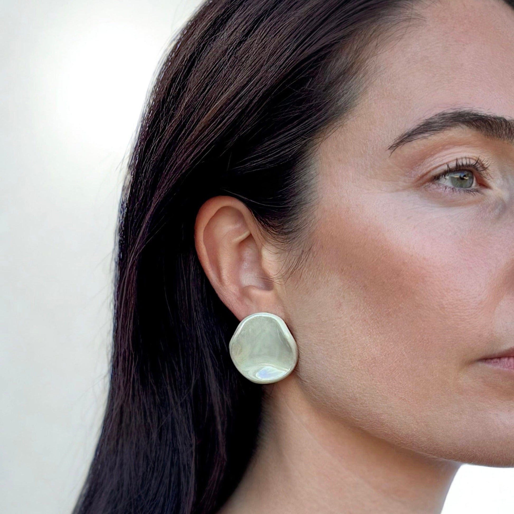 Sage-green ceramic stud earring with an organic rounded shape worn on a model's ear