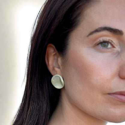 Closeup of a woman wearing a sage-green ceramic stud earring