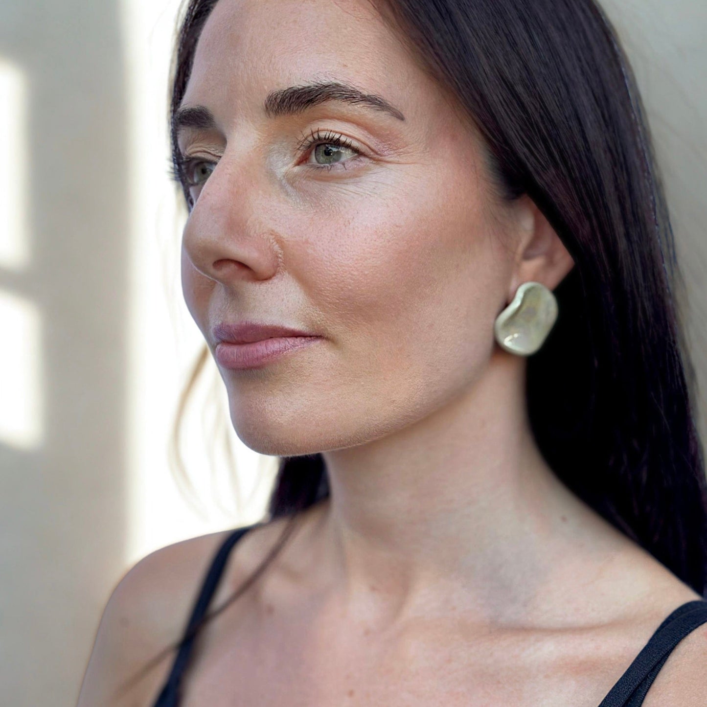 Profile view of a woman wearing the sage-green ceramic stud earring