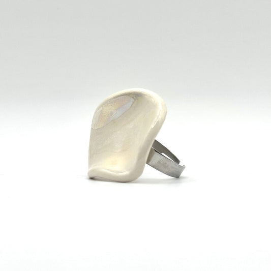 Pearl white ceramic ring on a finger against a bright blue sky and rocky landscape.