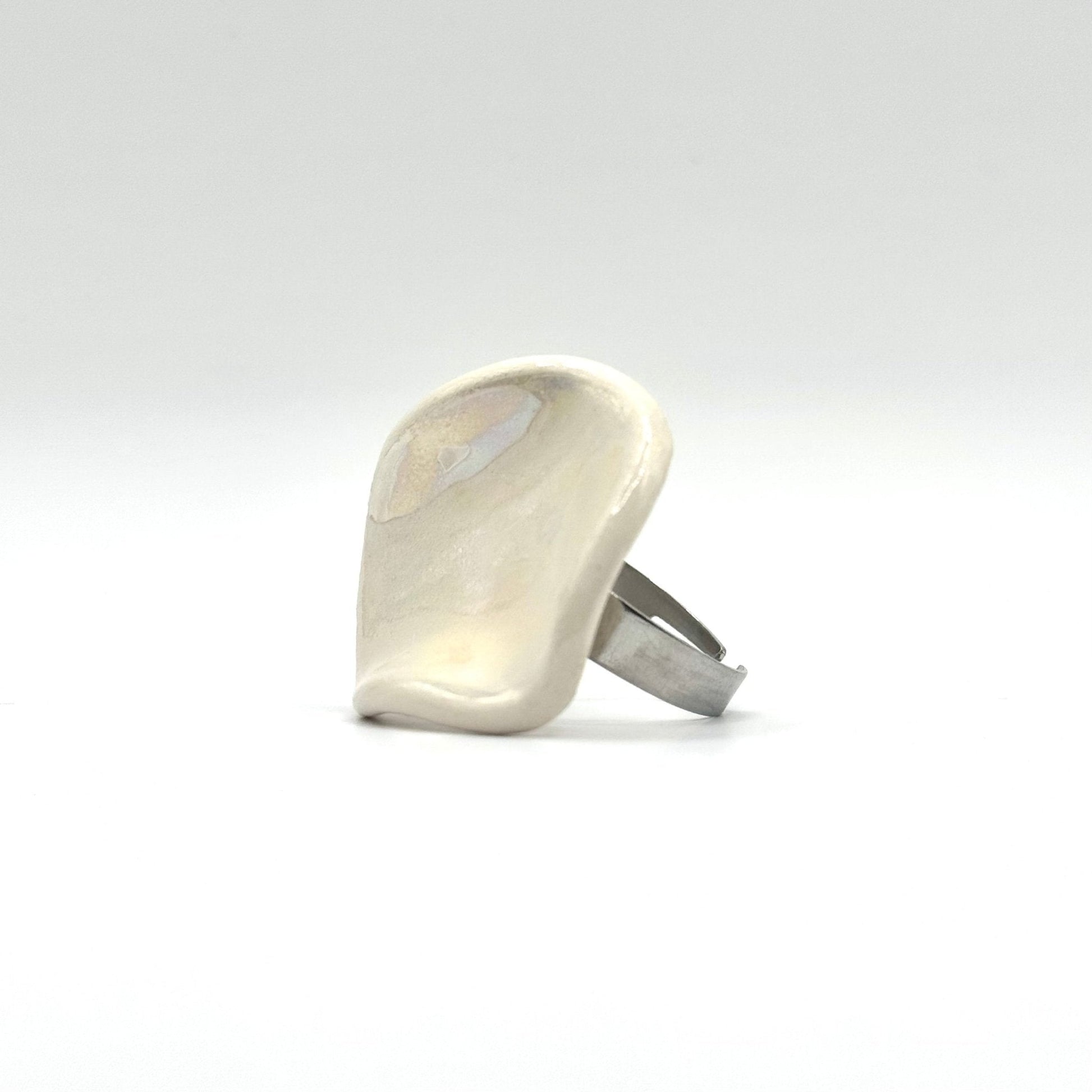 Pearl white ceramic ring on a finger against a bright blue sky and rocky landscape.