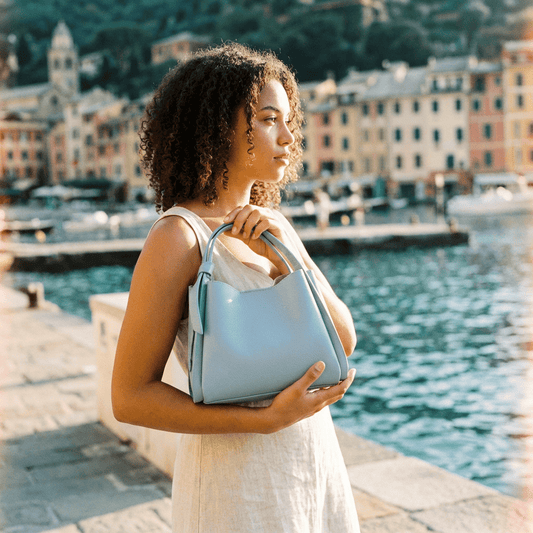 Woman by the harbor wearing a white dress carries a light blue Pienza Italian leather tote