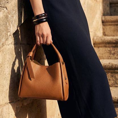 Person holding a brown handbag against a stone wall background