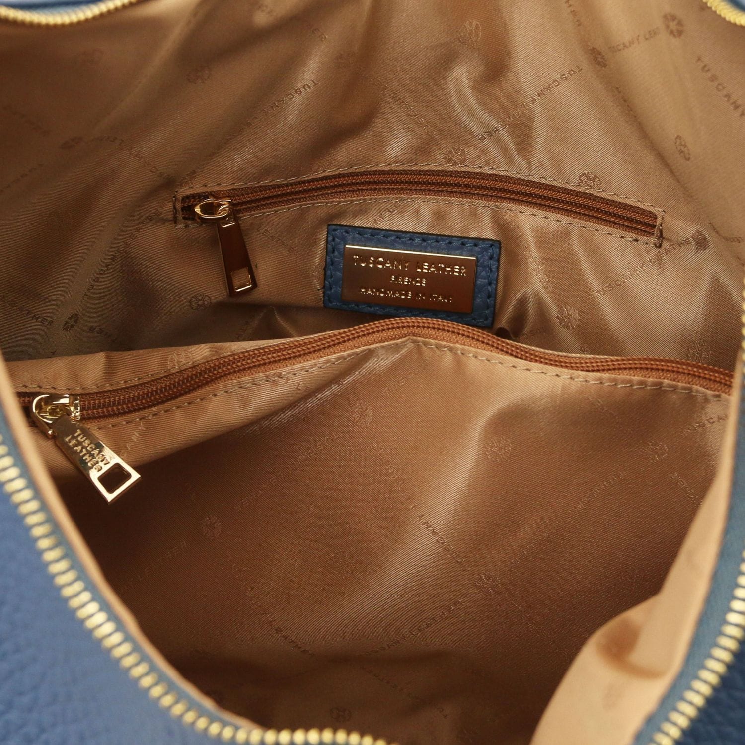 Interior of blue Italian leather bag with tan lining and zip pocket with branding plaque