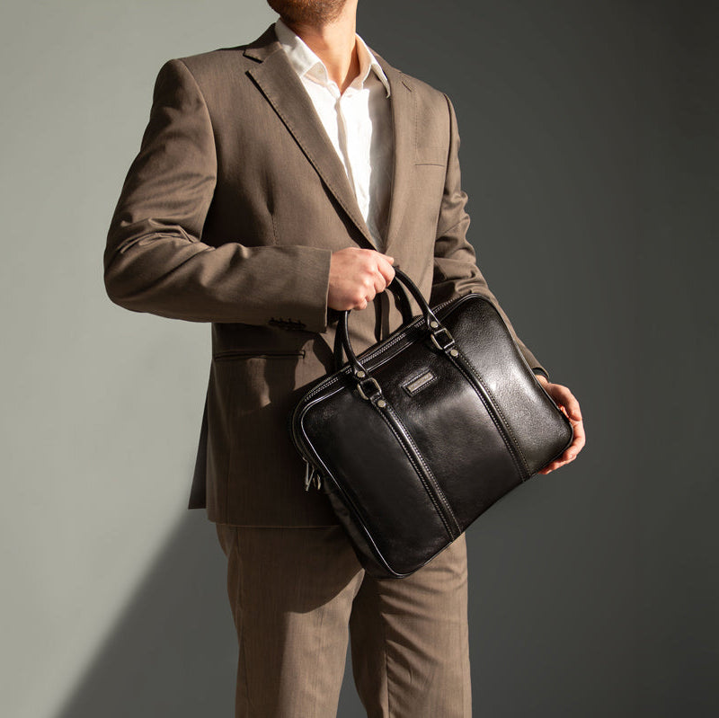 Man holding a black leather briefcase against a gray background