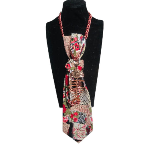 Patchwork fabric tie with a large jeweled pendant and red chain strap displayed on a black mannequin bust.