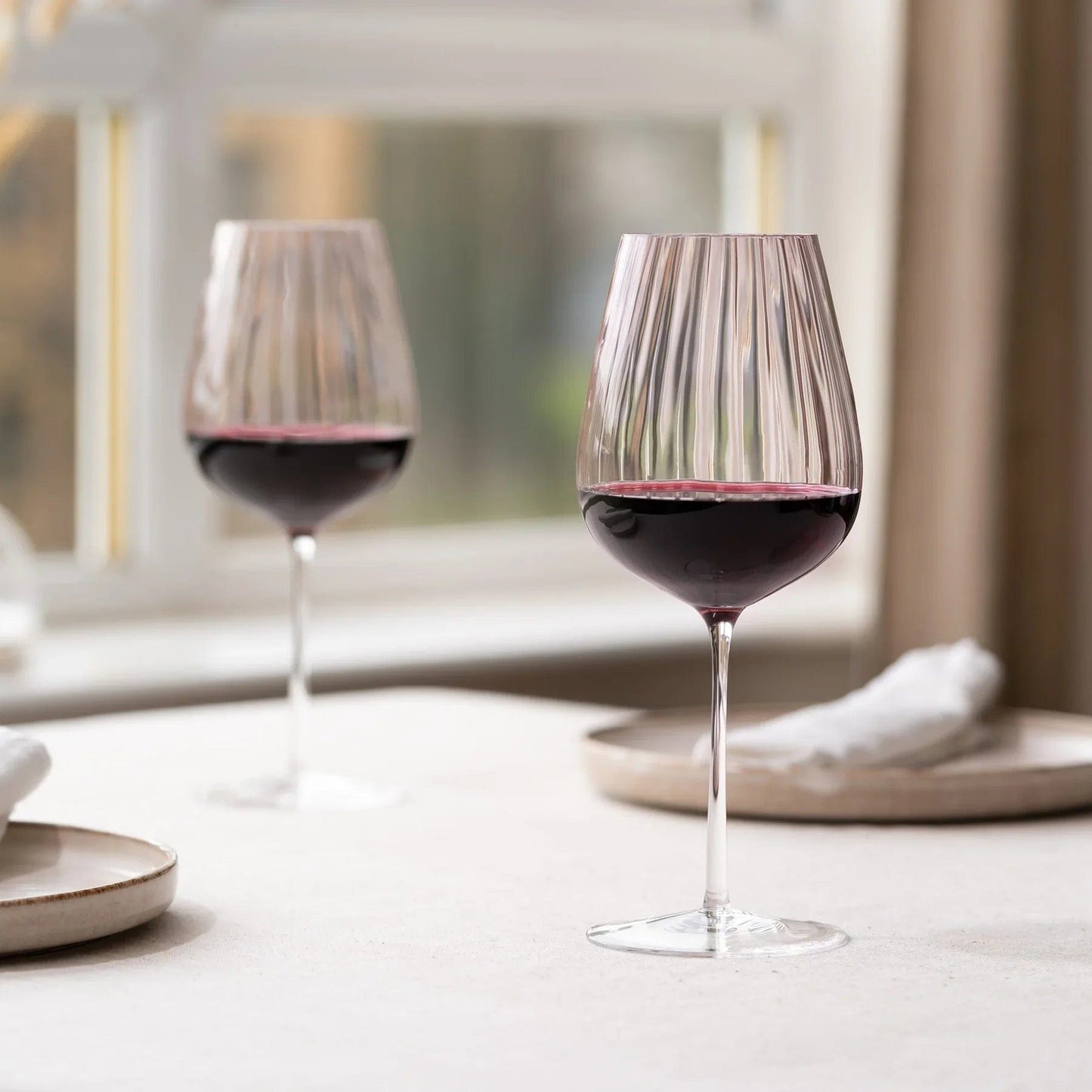 Two dusty rose ribbed wine glasses with red wine on a table