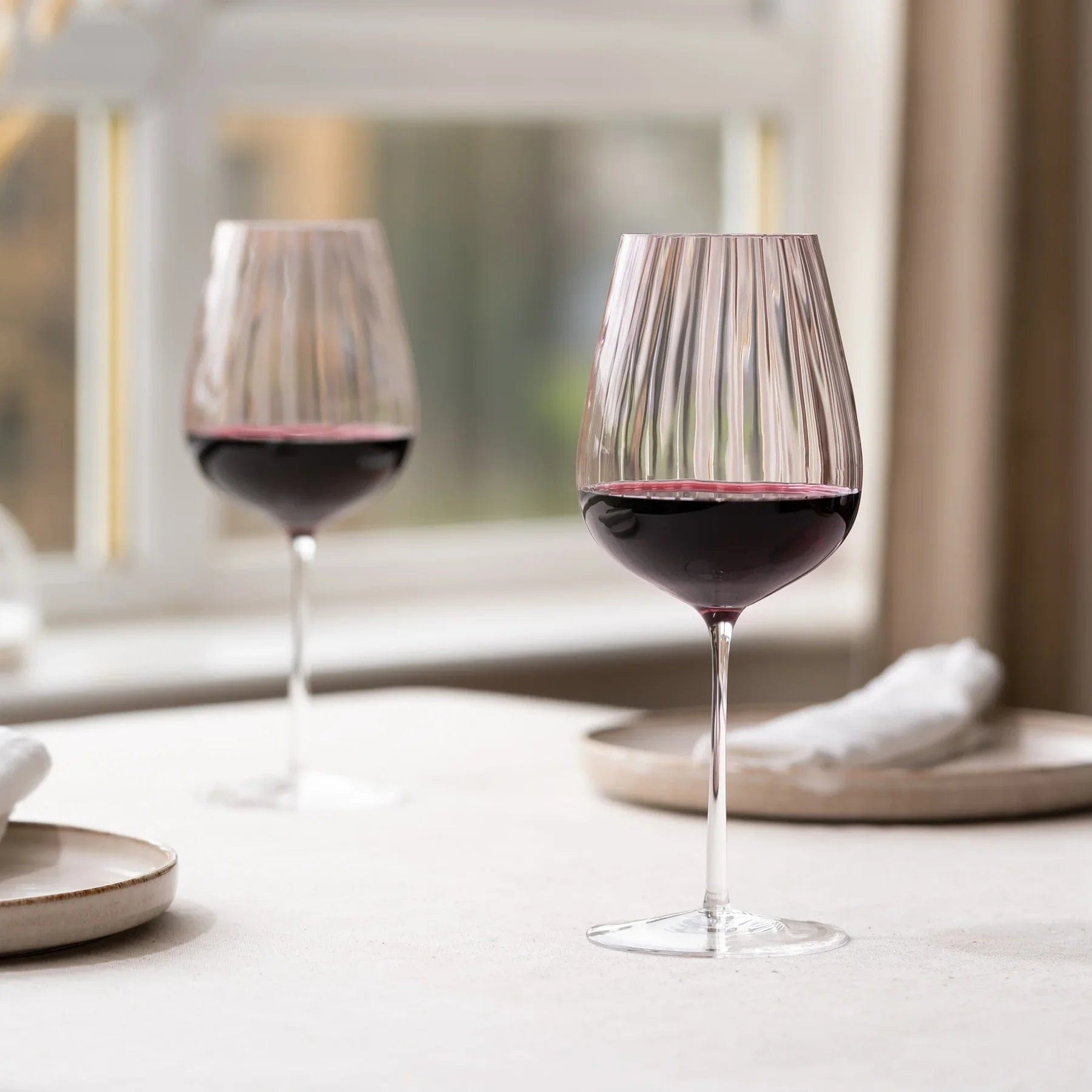 Two dusty rose ribbed wine glasses with red wine on a table