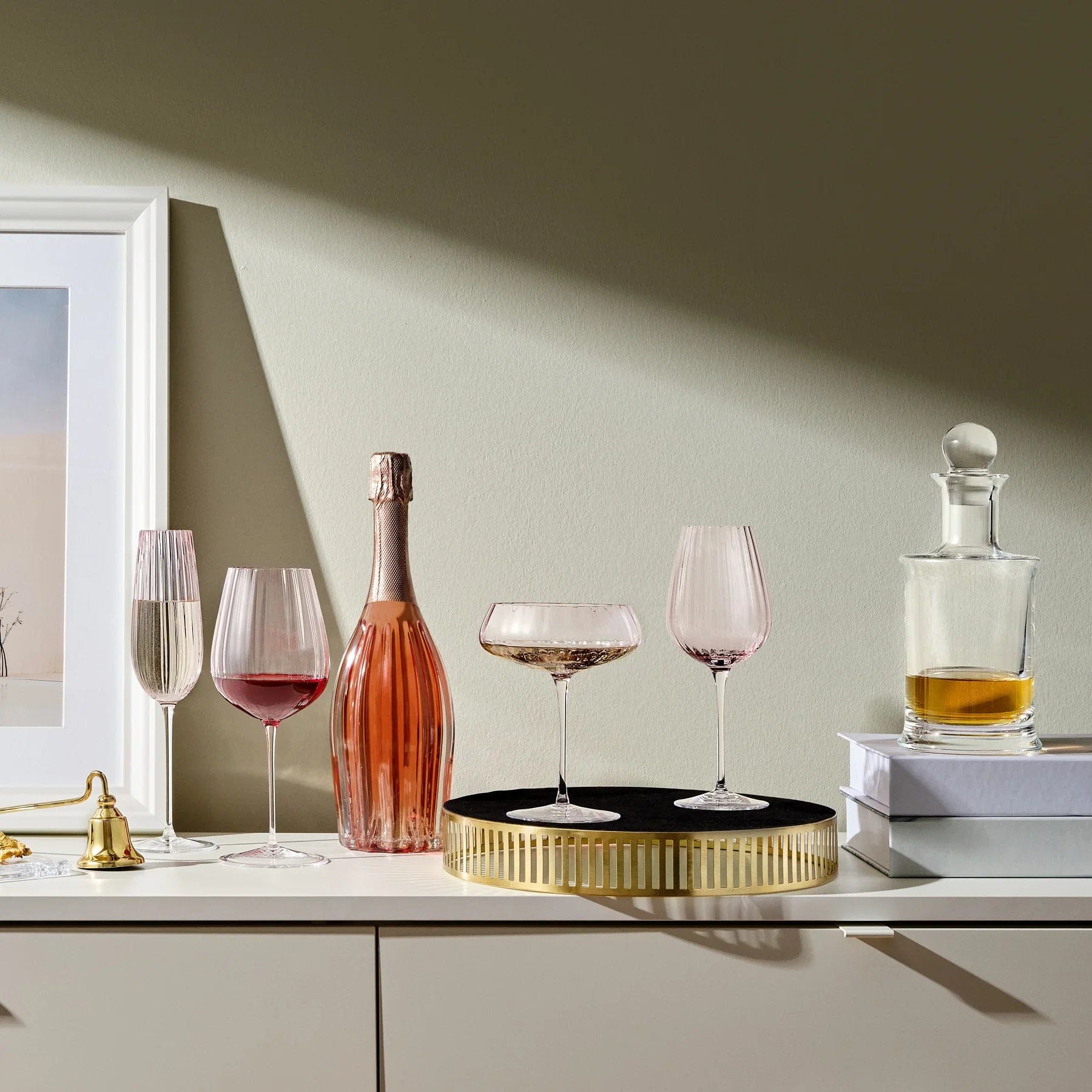 Round Up Dusty Rose glassware arranged on a white surface beside a pink champagne bottle and decorative items.