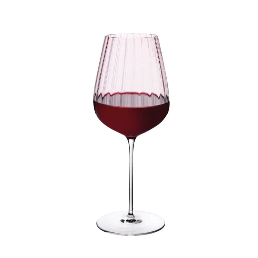 Dusty rose tinted red wine glass filled with wine against a white background