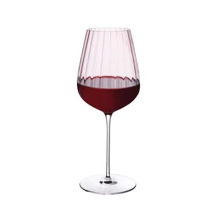 Dusty rose tinted red wine glass filled with wine against a white background