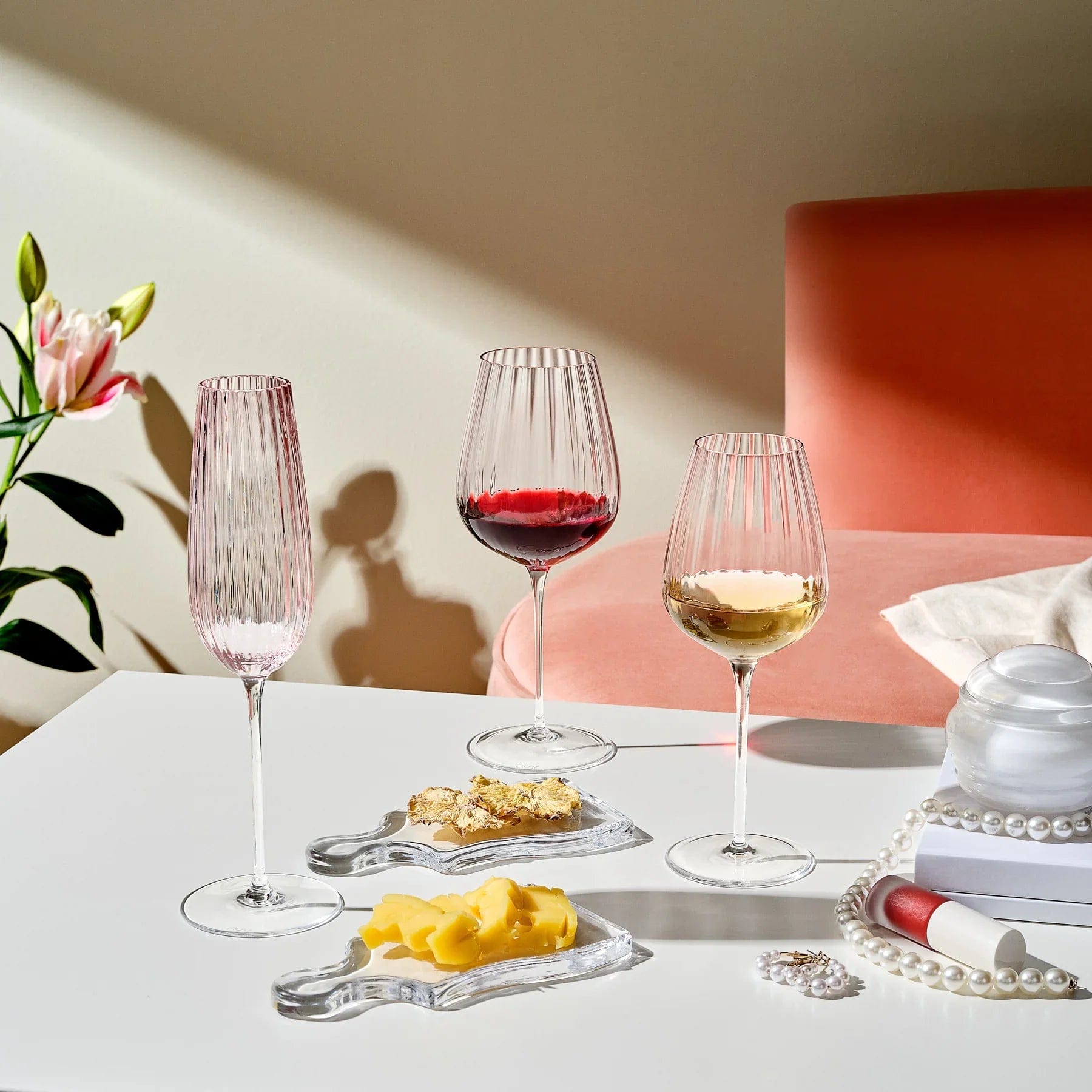 Round Up Dusty Rose glassware includes two red wine glasses and a champagne flute on a white table with cheese bites and pearls.
