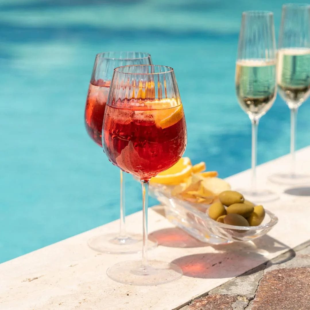 Two red wine glasses with a red cocktail and citrus wedge on a poolside table