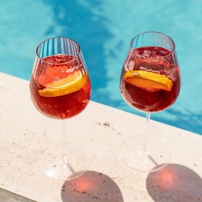 Two Round Up Dusty Rose red wine glasses with citrus slices in a poolside scene.