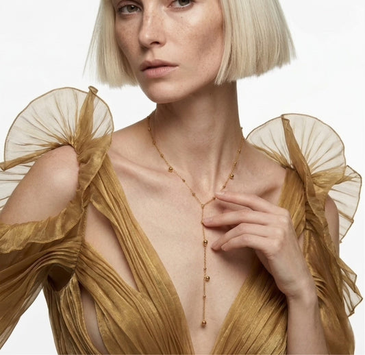 Woman wearing a gold dress with sheer sleeves against a white background