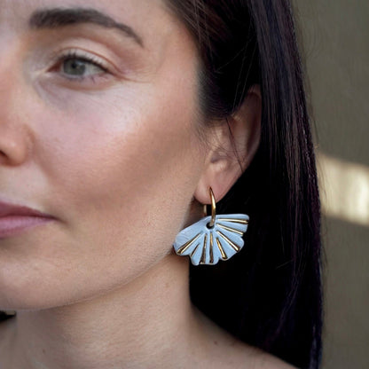 Woman wearing light blue fan shaped ceramic earrings with gold detailing
