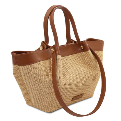 Side angle view of raffia tote with brown leather trim and long shoulder strap